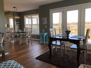 A dining area with a table and chairs, a chandelier, and a view through large windows.