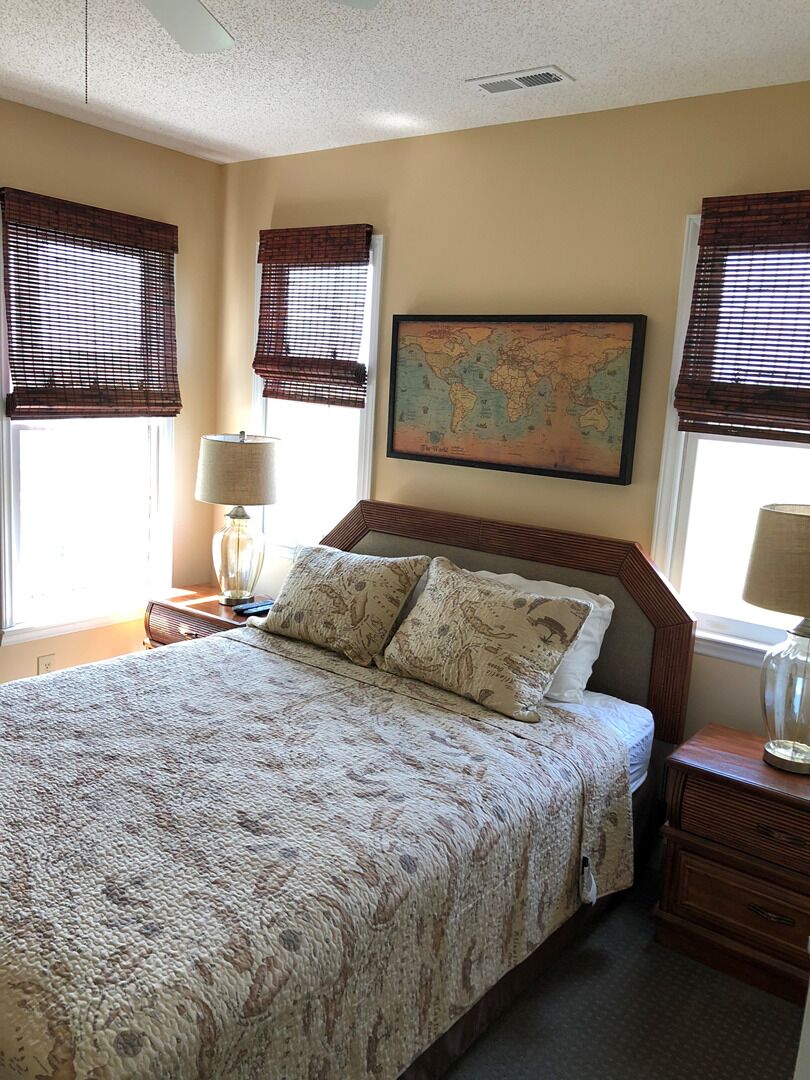 A bedroom with a large bed, two bedside tables, a map on the wall, and window treatments.