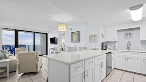 A modern kitchen with white cabinetry, a large island, and a dining area with a sofa and chairs.