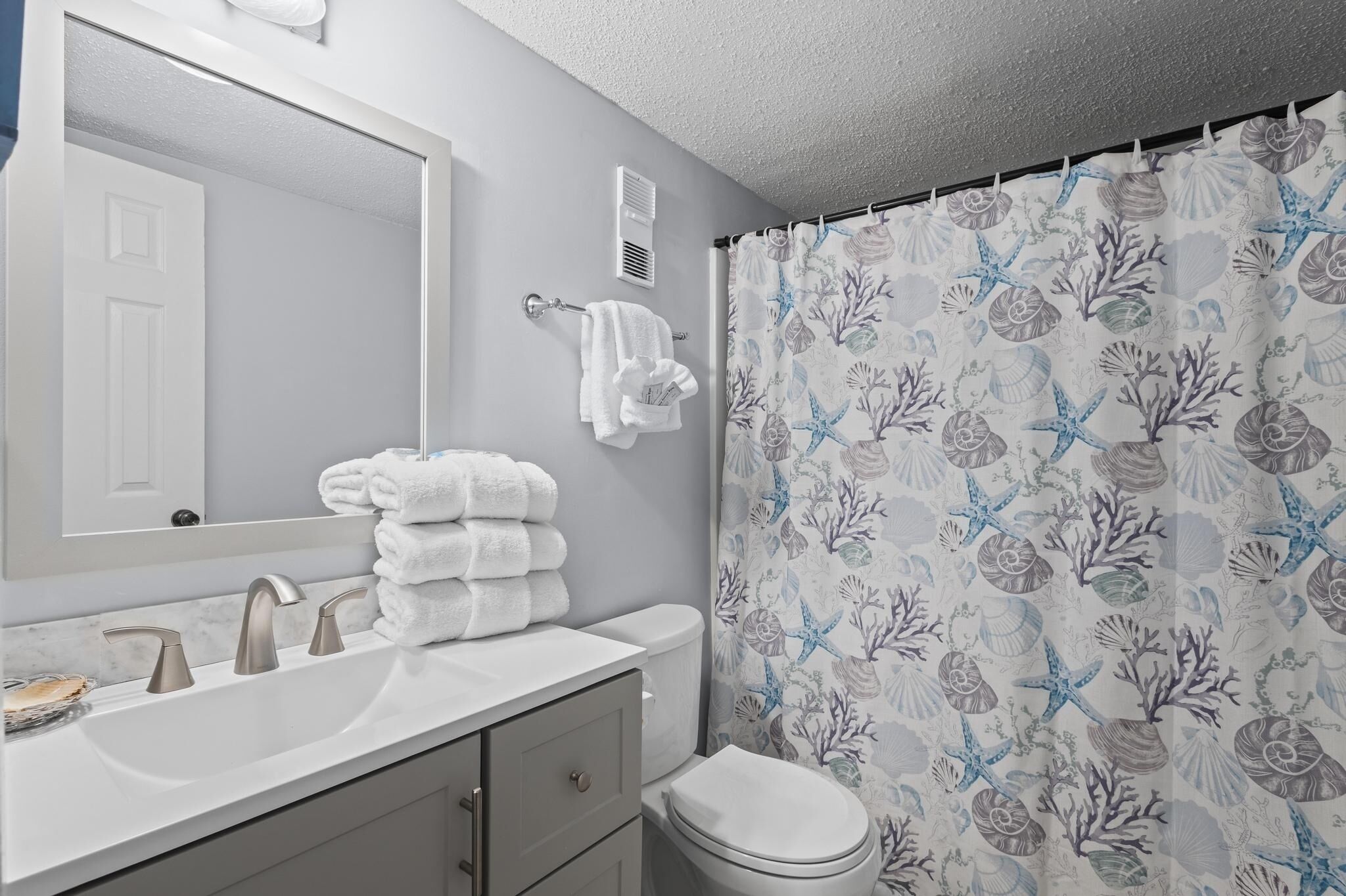 Une salle de bain avec un lavabo blanc, deux robinets, un miroir, un porte-serviettes avec des serviettes pliées et des toilettes.