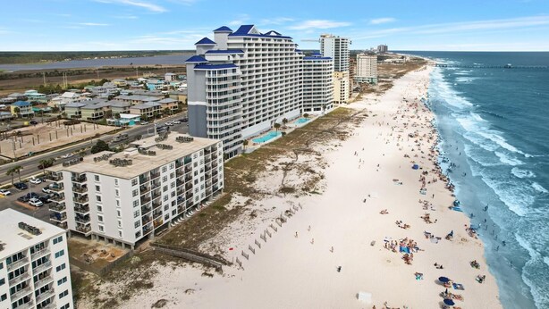 A beachfront hotel with multiple floors, a pool area, and a sandy beach.