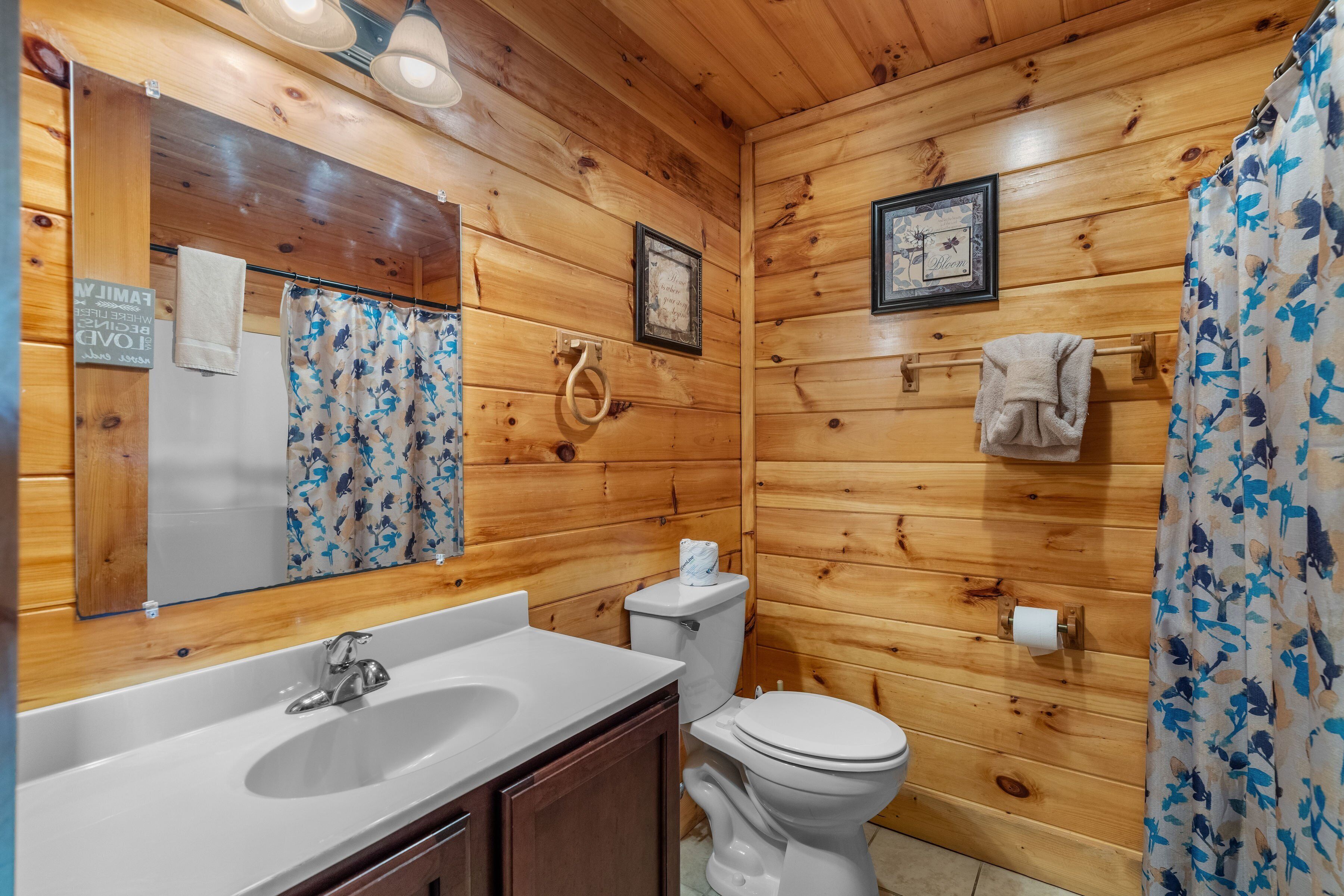 A wooden cabin bathroom with a sink, toilet, and shower curtain.
