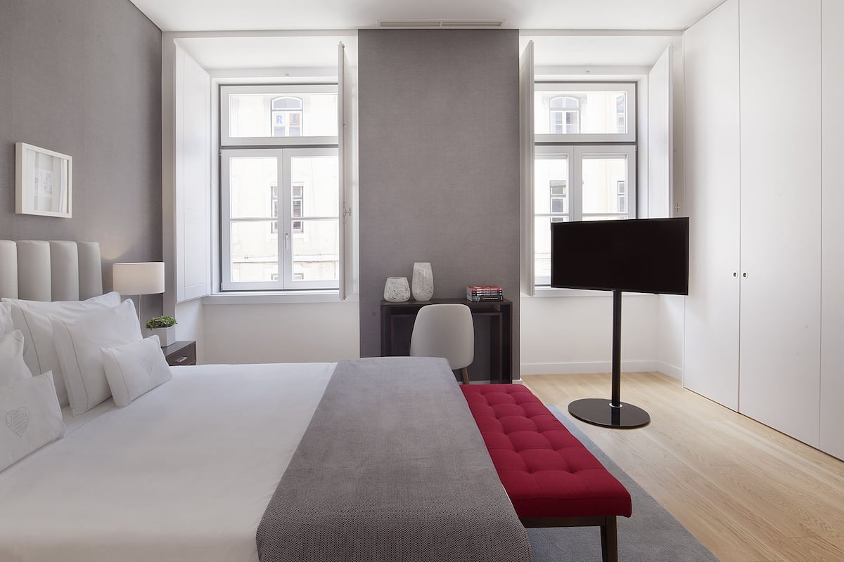 A modern bedroom with a large bed, a flat-screen TV, and a bench.