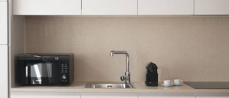 Una cocina moderna con microondas integrado, lavamanos de acero inoxidable y cafetera.