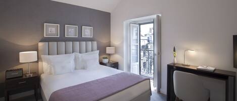 A modern hotel room with a large bed, bedside lamps, a desk with a chair, and a balcony with a view.