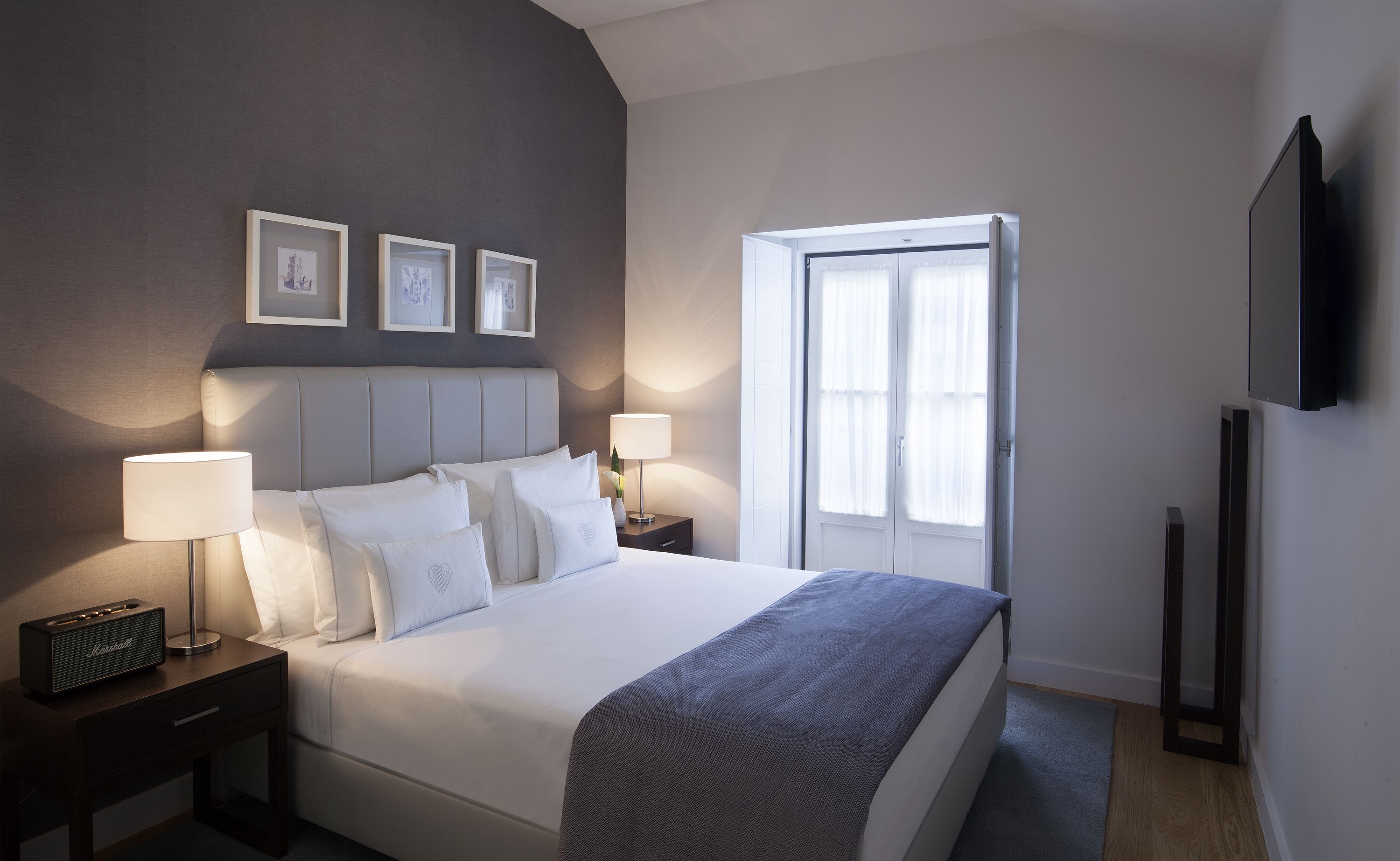 A hotel room with a large bed, bedside lamps, a flat-screen TV, and framed pictures on the wall.
