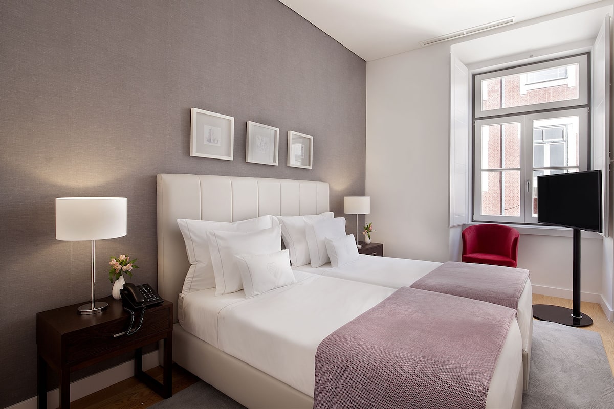 A hotel room with a large bed, bedside tables, a TV, a red chair, and framed pictures on the wall.