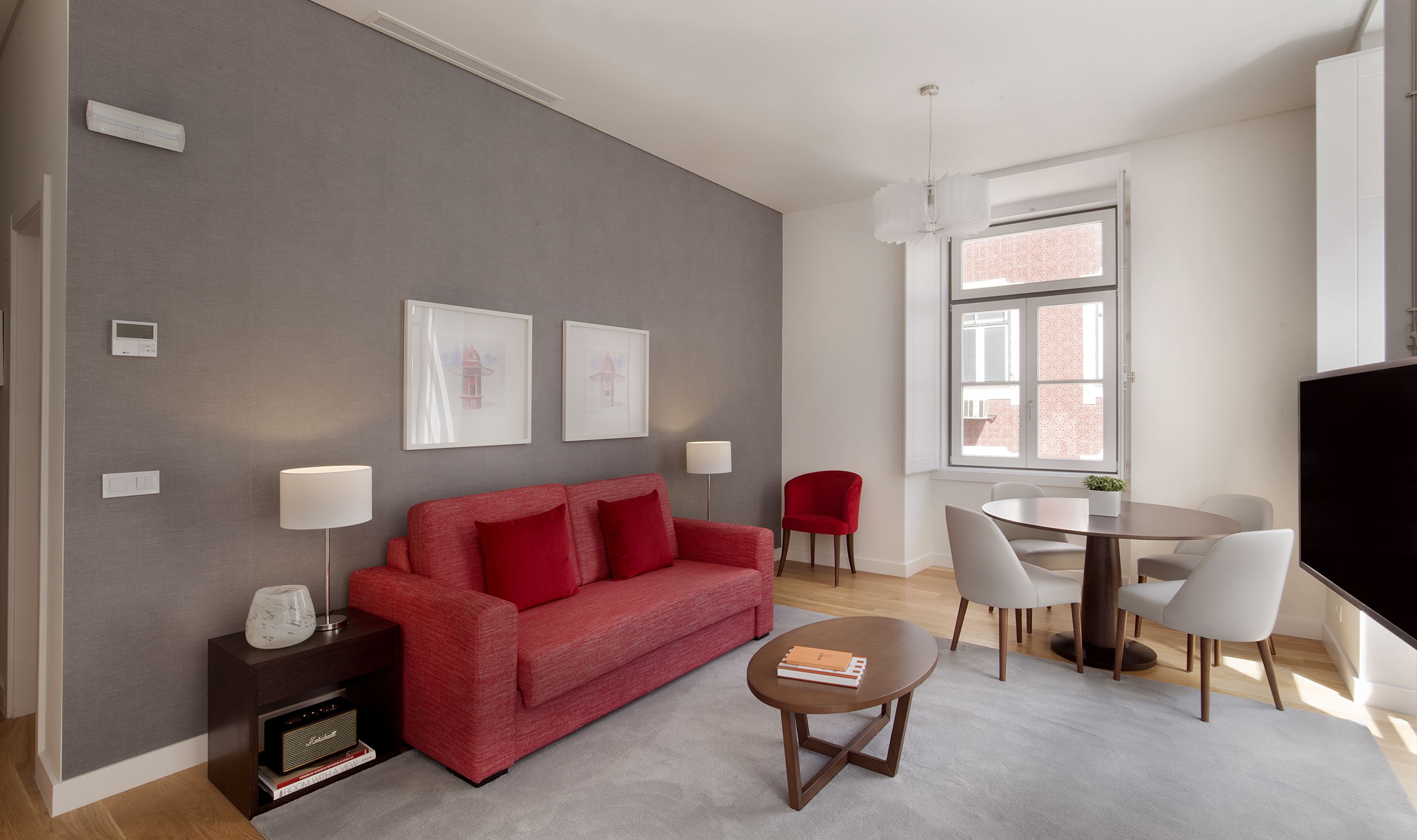 Una sala de estar moderna con una pared gris, sofá rojo y un comedor con mesa y sillas redondas.