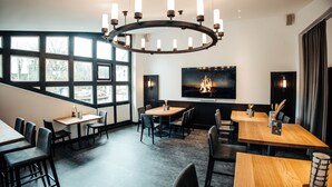 Un comedor moderno con una gran pantalla de televisión, un candelabro circular y varias mesas y sillas.