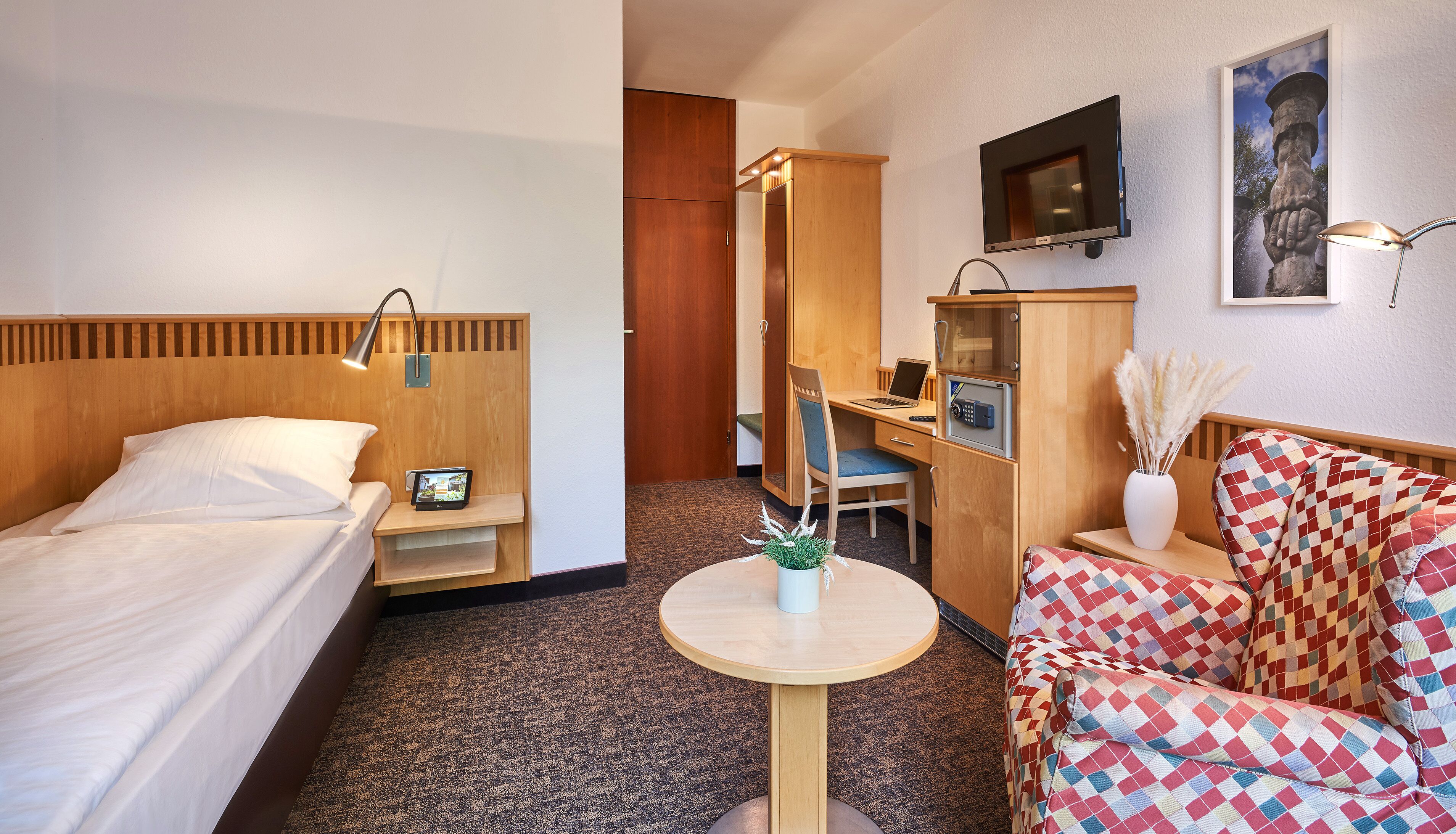 Een hotelkamer met een bed, bureau, stoel en een klein tafeltje met een plant.