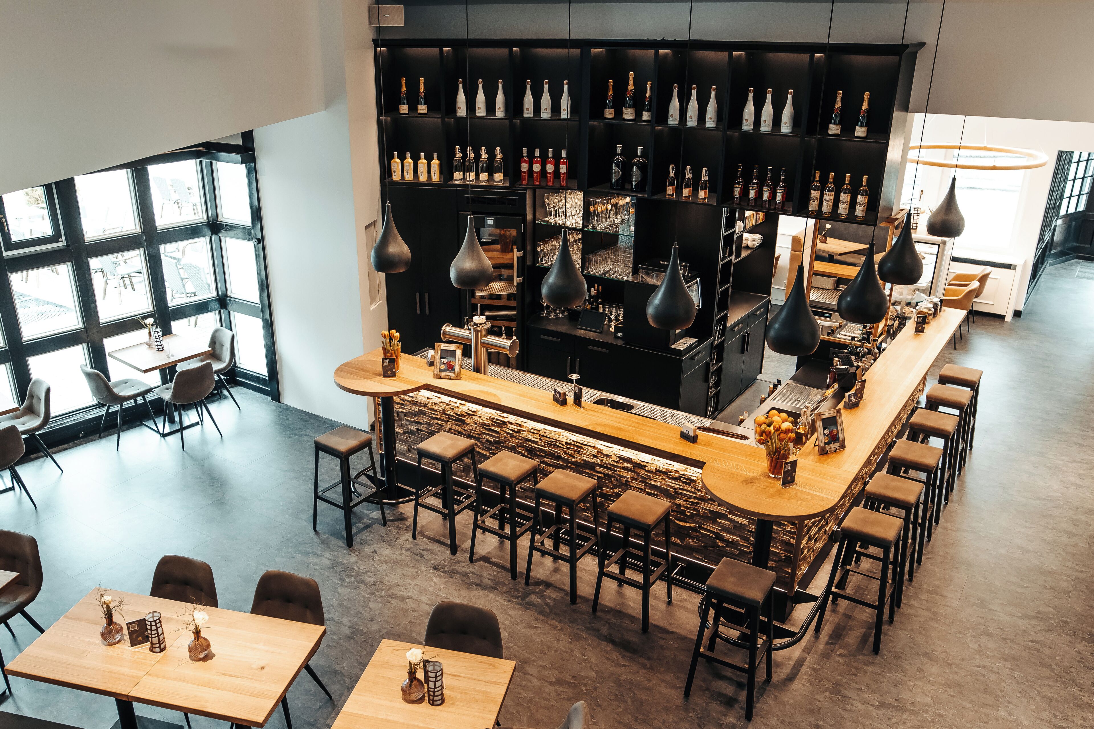 A modern bar area with a long counter, multiple stools, and a variety of bottles and glasses on shelves.