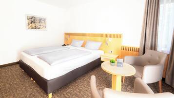 Une chambre d’hôtel avec un lit, une table de chevet, une chaise et une petite table sur laquelle est posée une plante.
