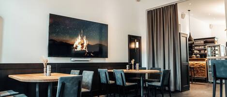 A modern hotel room with a large TV displaying a starry night scene, a cozy fireplace, and a bar area in the background.