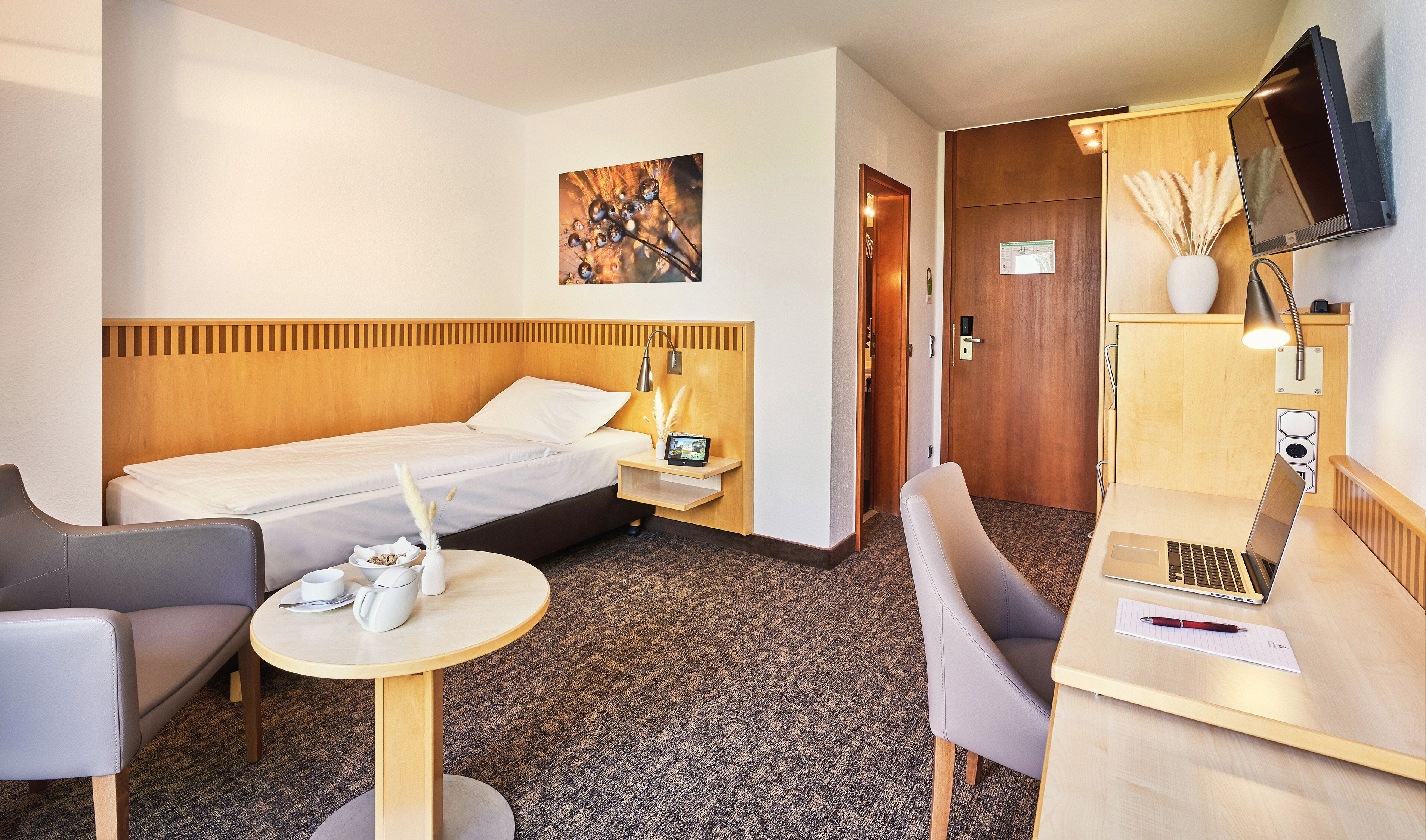Une chambre d’hôtel avec un lit, un bureau, une chaise, une petite table, un téléviseur et un tableau au mur.