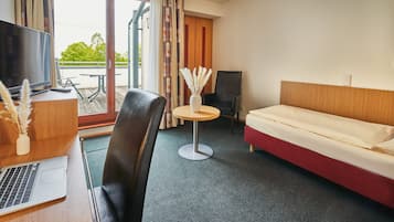 Habitación de hotel con una cama, un escritorio con una computadora portátil, una silla, una mesita con un jarrón y un televisor.