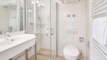Un baño moderno con ducha envuelta en vidrio, un lavamanos blanco y un inodoro.
