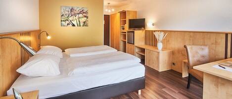 Une chambre d’hôtel avec un lit, des tables de chevet, un bureau, une chaise, une télévision et un tableau au mur.