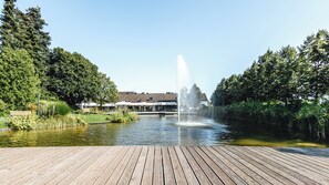 Une terrasse en bois avec une fontaine au centre, entourée d’eau et de verdure.