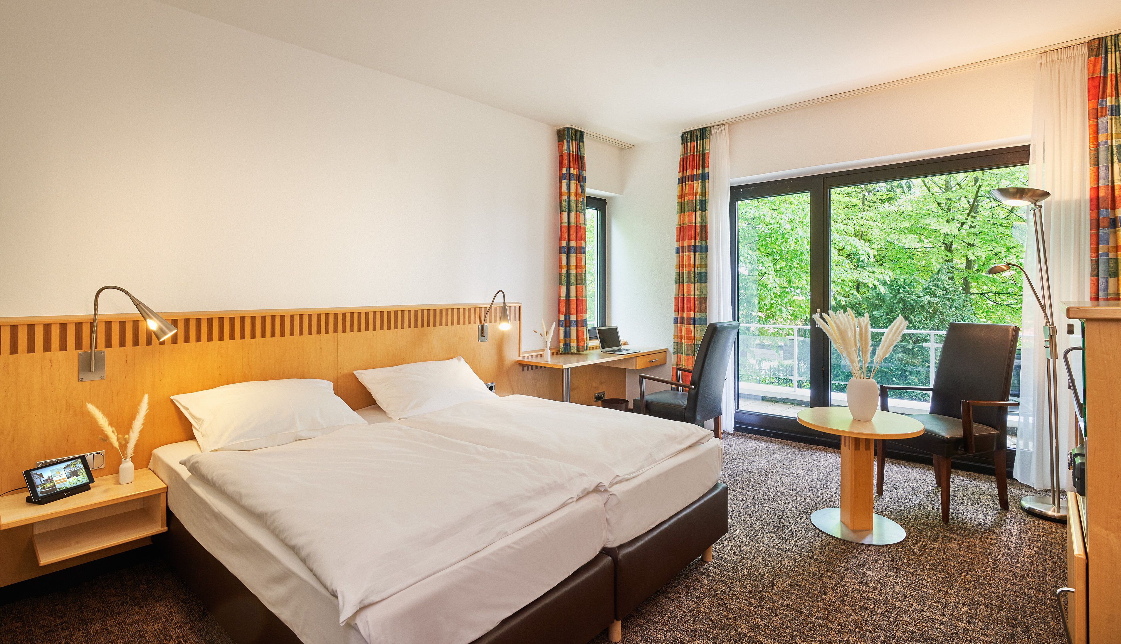 Habitación de hotel con cama, escritorio, silla y vistas al exterior con vegetación.