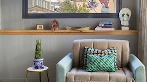 Une pièce confortable avec un canapé, une petite table d’appoint, une plante en pot et une fenêtre donnant sur des immeubles.