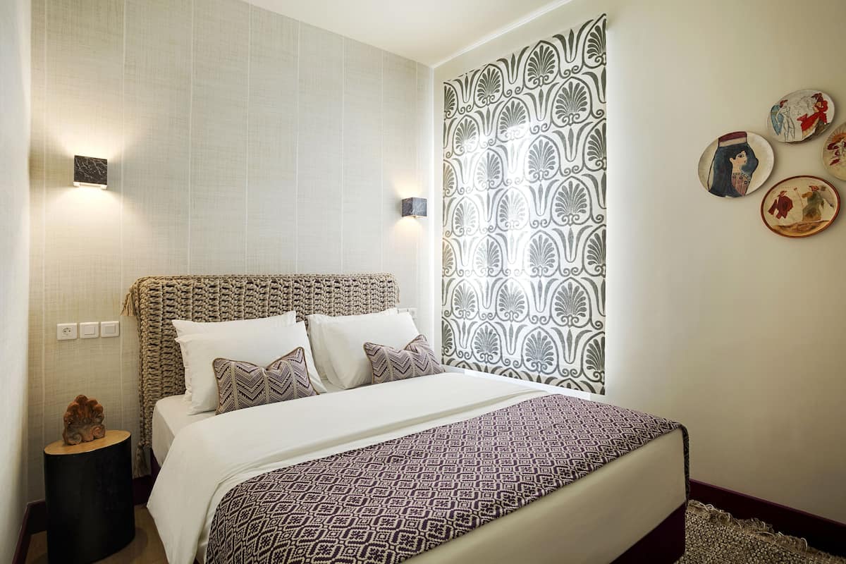 Um quarto bem arrumado com cabeceira estampada, cama com roupa de cama estampada, mesa de cabeceira e pratos decorativos na parede.