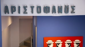 Une enseigne portant l’inscription « APIOTHANUE » et une œuvre d’art rouge représentant quatre personnages portant des chapeaux.
