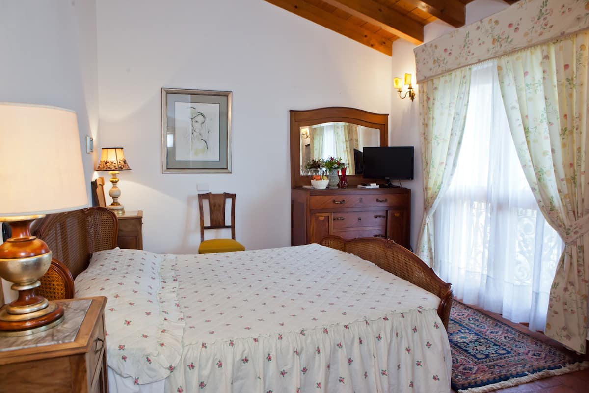 Quarto com cama, cômoda de madeira, televisão, cadeira e luminária.