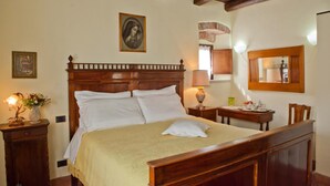 Un dormitorio con una cama de madera, una mesita de noche con una lámpara, un retrato enmarcado y un espejo en la pared.