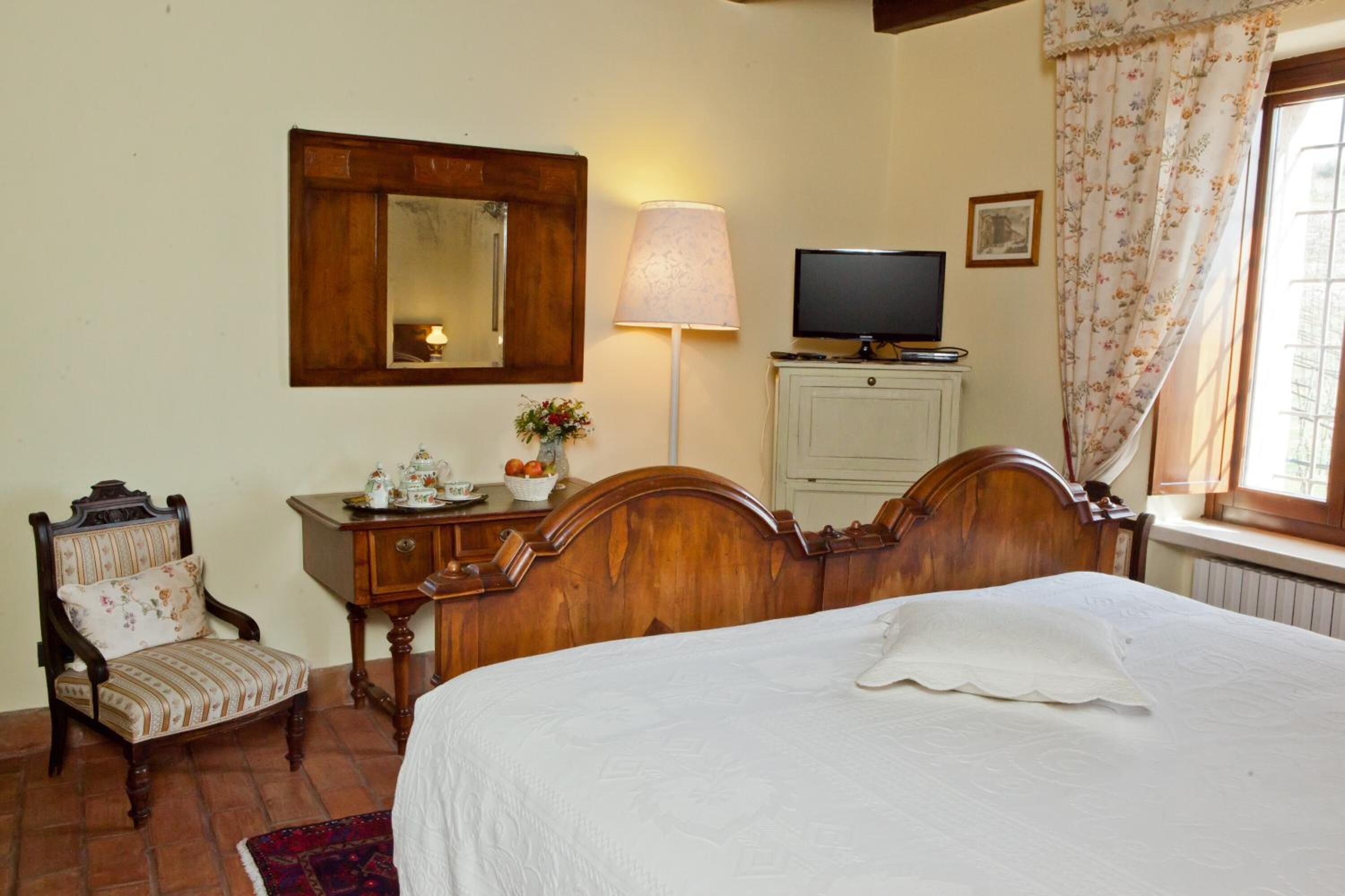 Une chambre à coucher avec un lit en bois, une chaise, une commode, un téléviseur et une fenêtre avec des rideaux.