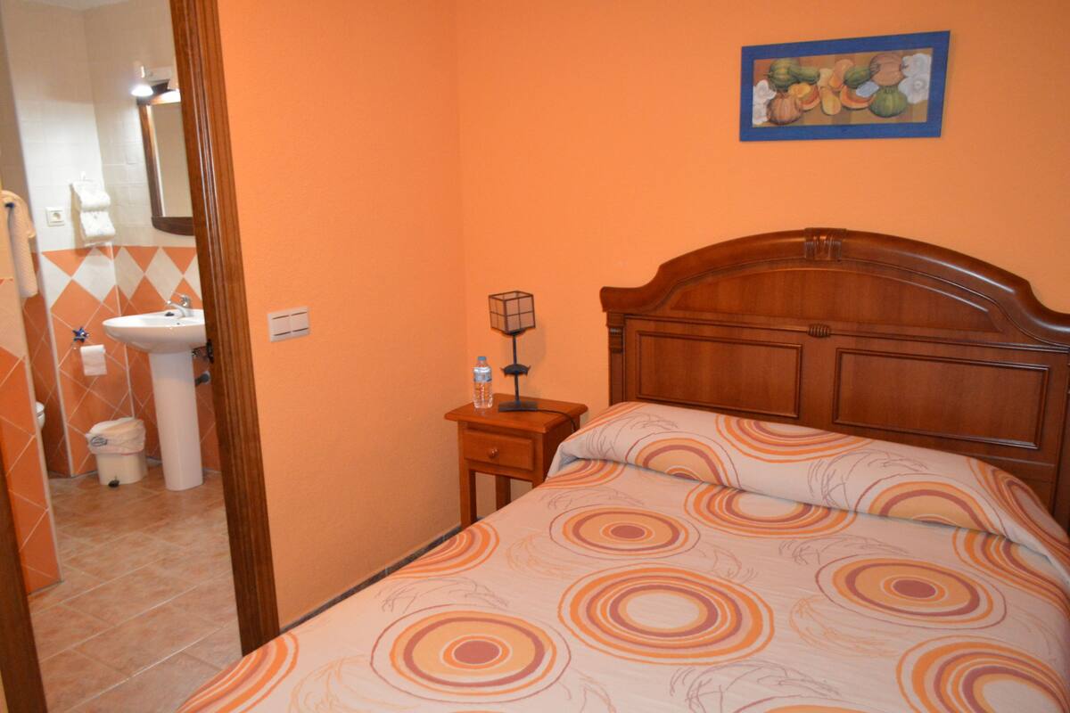 Une chambre à coucher avec une tête de lit en bois, un lit recouvert d’une couvre-lit à motifs, une table de chevet avec une lampe et un tableau accroché au mur.