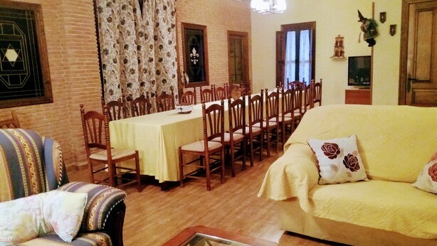 A dining area with a long table and chairs, a sofa, and a patterned armchair. - Posada la Reja (Malpica de Tajo)