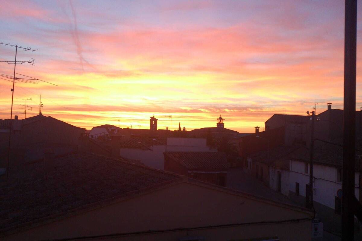 Une vue sur le coucher de soleil au-dessus d’une ville, avec ses bâtiments et le clocher d’une église.