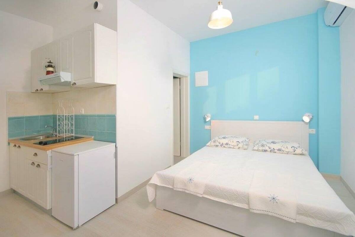 Habitación pequeña con cama, una kitchenette y una pared azul.