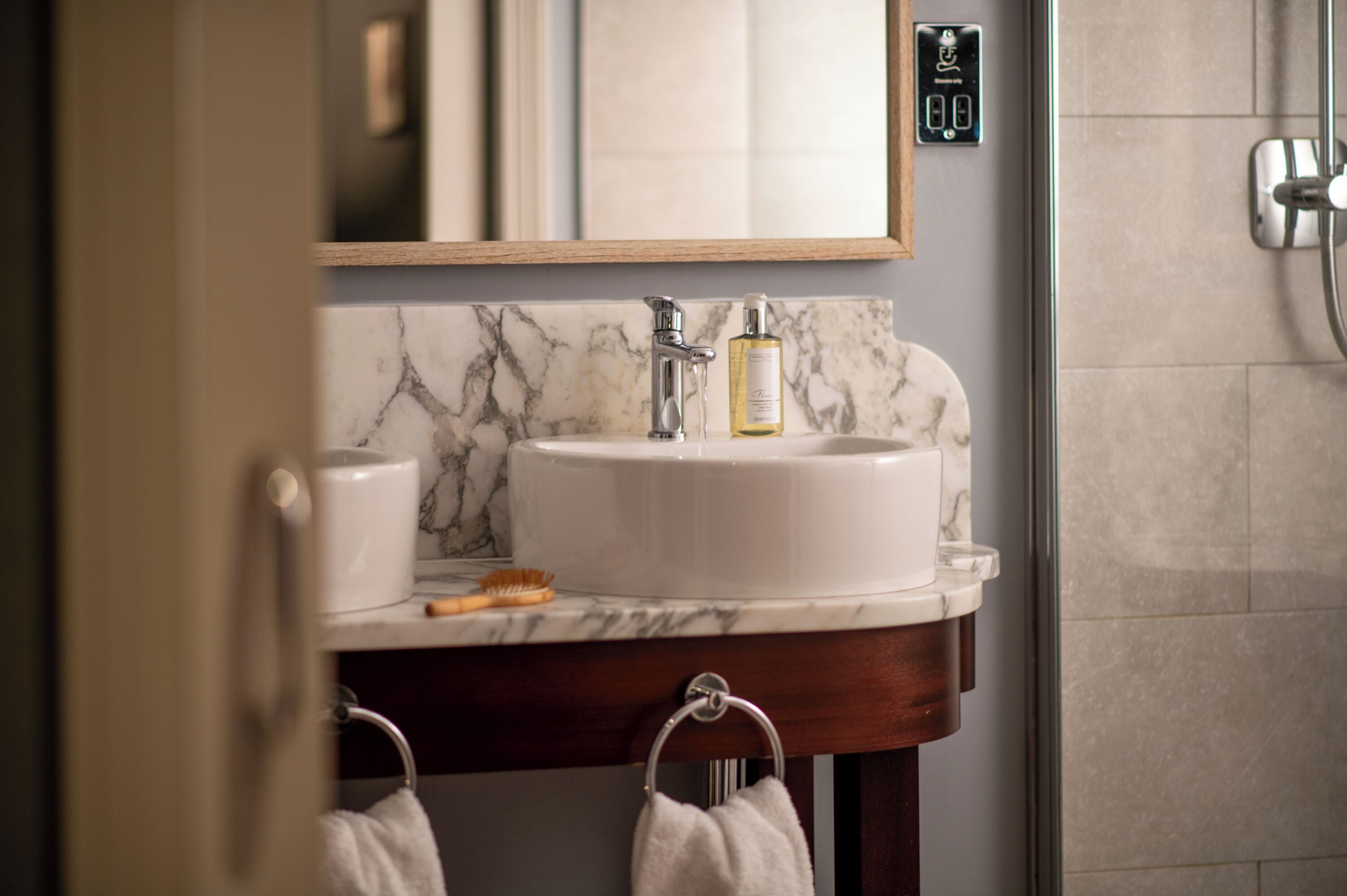 A bathroom with a marble sink, a mirror, a towel ring, and a shower area.