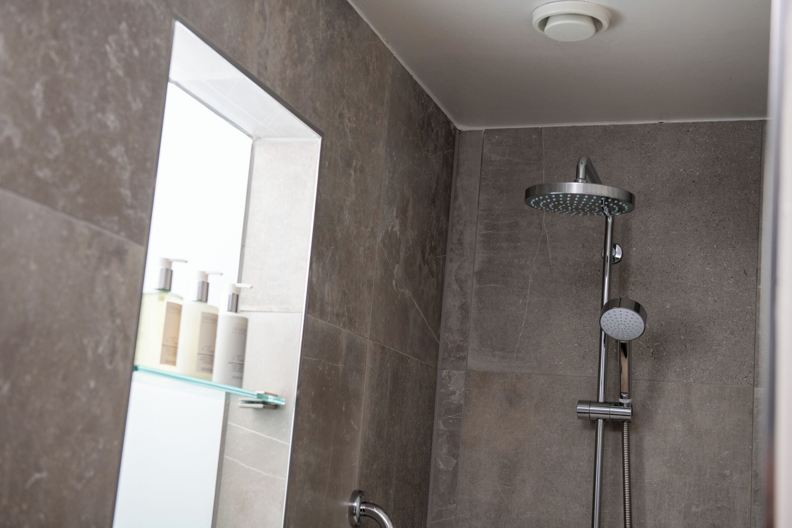 A modern shower with a handheld showerhead and a wall-mounted rain showerhead.