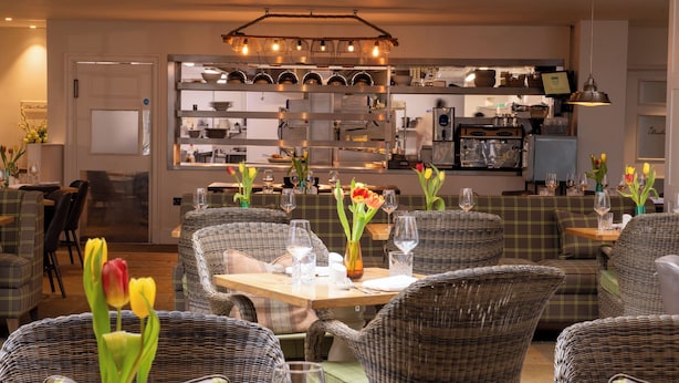 A restaurant with wicker chairs, a wooden table, and vases with flowers. - Beverley Arms Hotel (Beverley)