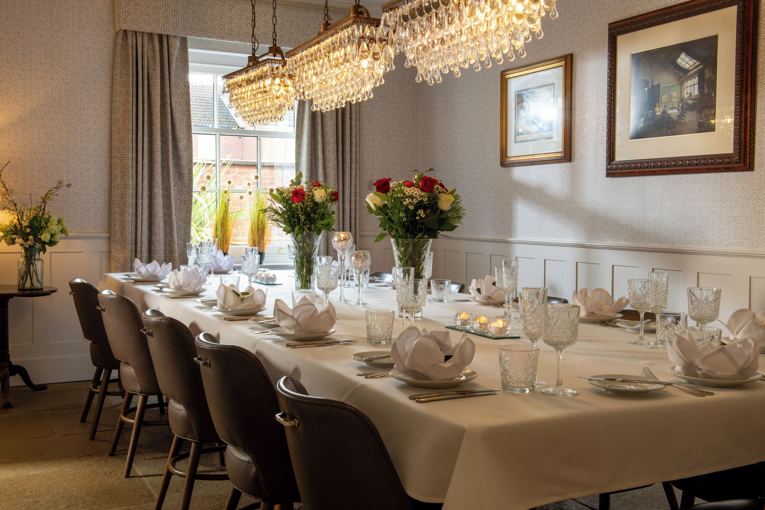 Een lange eettafel gedekt voor een formeel diner, met stoelen, kaarsen en bloemstukken als decoratie.