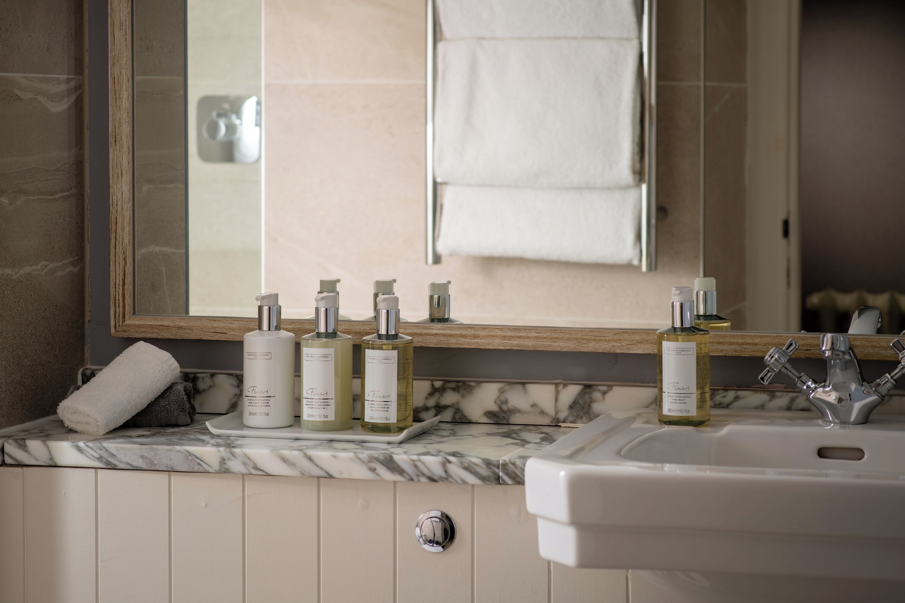 A bathroom with a marble countertop, a sink, and a mirror. There are three bottles of lotion and a towel on the counter.