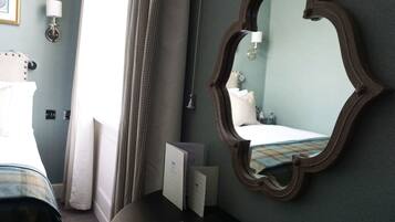 Habitación de hotel con una cama, una mesita de noche con lámpara, un espejo y una ventana con cortinas.
