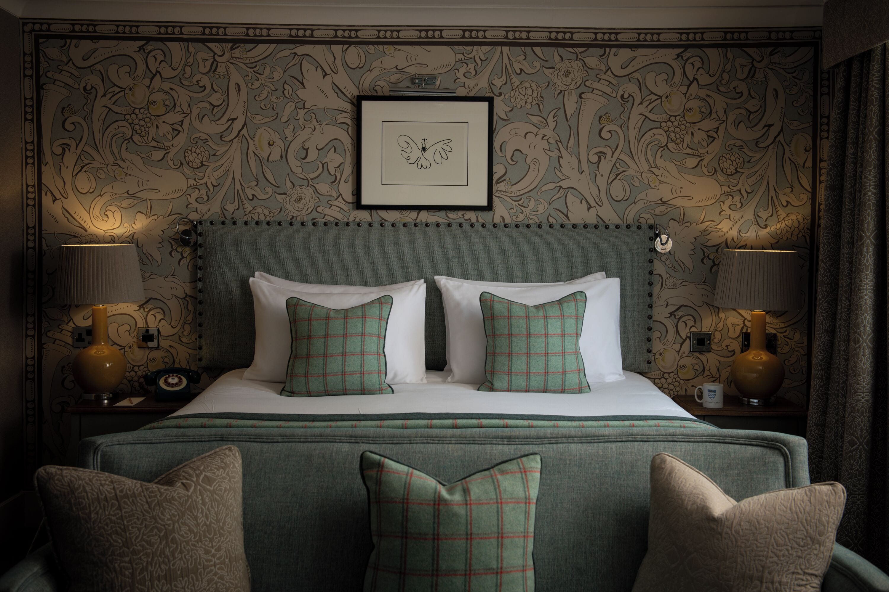 A neatly made bed with plaid pillows, a framed floral artwork above it, and two bedside lamps on either side.