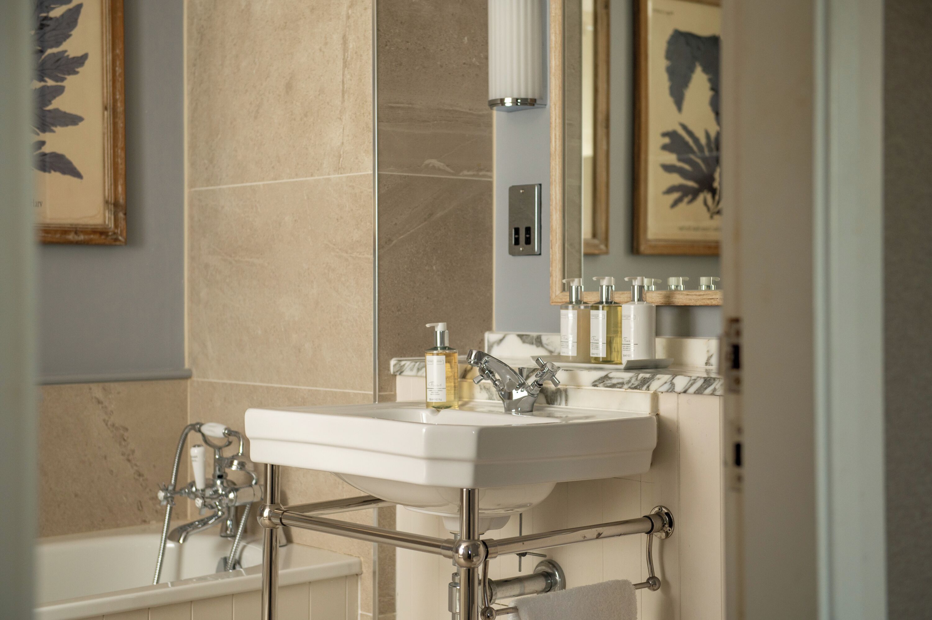 A bathroom with a white sink, a bathtub, and a mirror. There are framed pictures on the wall.