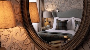 A bedroom with a bed, a nightstand, a lamp, a mirror, and a floral wallpaper pattern. - Beverley Arms Hotel (Beverley)
