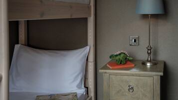 Een stapelbed met een witte matras, een klein nachtkastje met een lamp, en een speelgoeddinosaurus op het tafeltje.