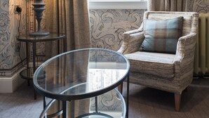 A room with a round glass table, a cushioned armchair, a lamp, and a window with a view of a historic building. - Beverley Arms Hotel (Beverley)