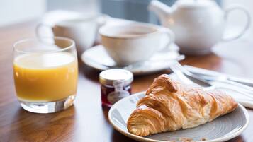 Un desayuno con un croissant, un vaso de zumo de naranja y una tetera sobre una mesa de madera.