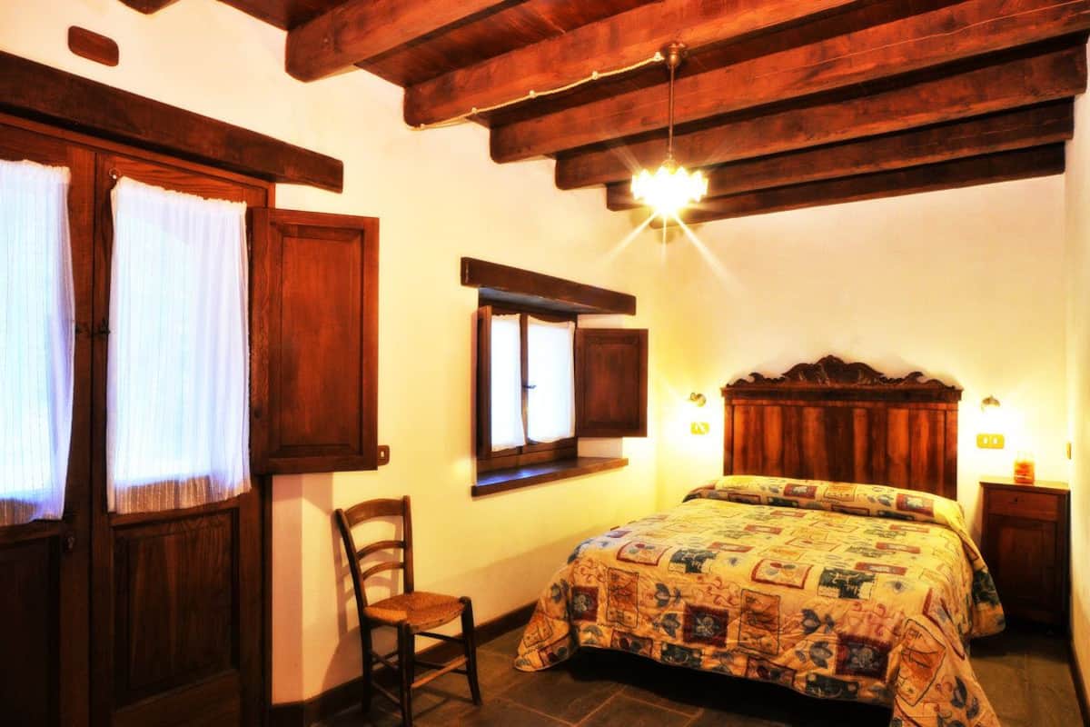 Un dormitorio acogedor con techo de madera, una cama con colcha estampada, una silla y una mesita de noche con lámpara.