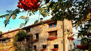 Un bâtiment en pierre doté de nombreuses fenêtres et de balcons, entouré d’une végétation luxuriante et de fleurs.
