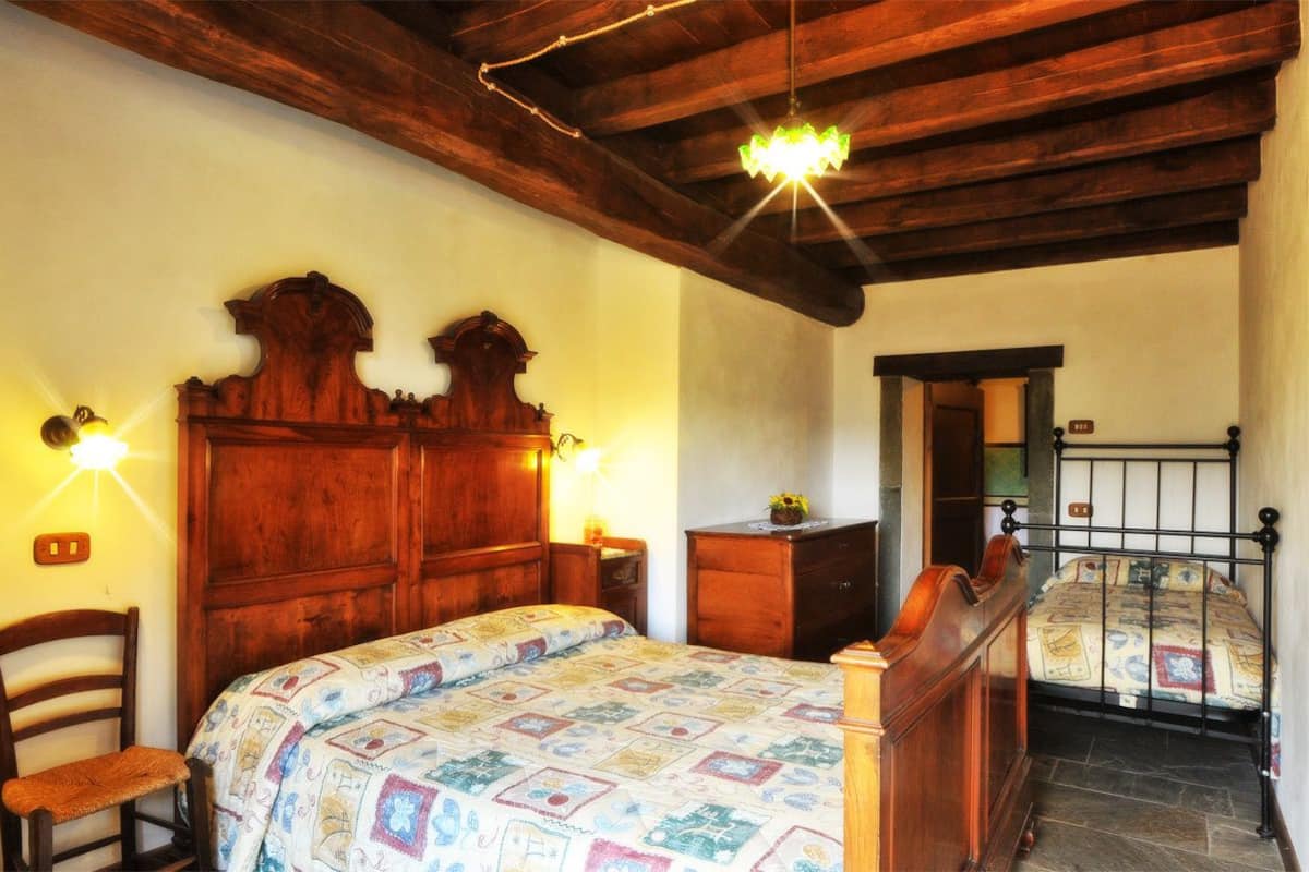 Un dormitorio con una cama de madera, una mesita de noche, una silla y un aparador.  Hay una araña colgando del techo.