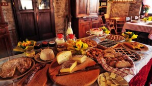 Une table garnie de divers fromages, pains et pâtisseries, dans un décor rustique avec des meubles en bois et un mur de pierre.