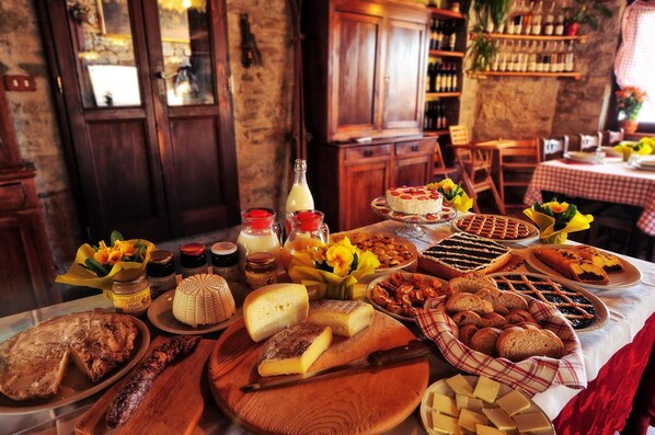 A table with various cheeses, breads, and pastries in a rustic setting with wooden furniture and a stone wall.